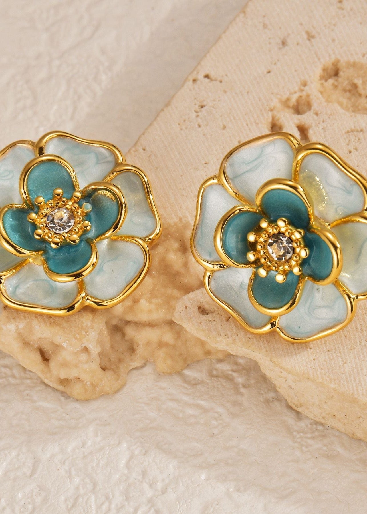 Floral earrings with gold and teal design on a textured beige background