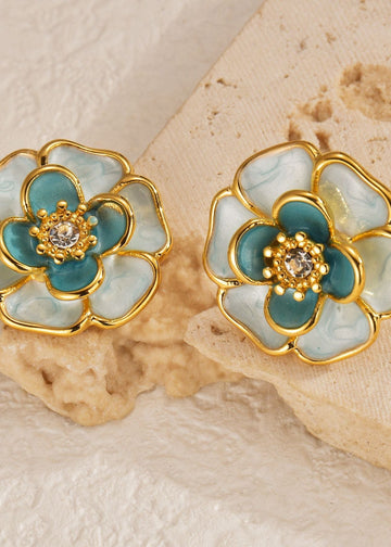 Floral earrings with gold and teal design on a textured beige background